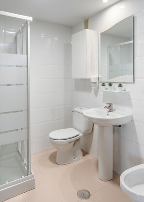 A modern bathroom with a glass shower enclosure, a toilet, a sink, and a mirror. - Apartamentos Alday (Camargo)