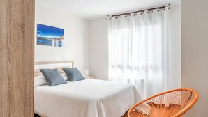 Quarto com cama, cadeira, quadro na parede e janela com cortinas.