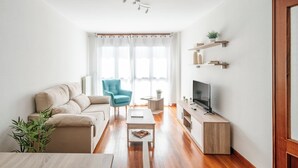 Uma sala de estar moderna com um sofá, uma poltrona azul, uma mesa de centro, uma TV e estantes de madeira.