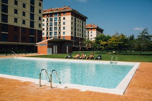 A swimming pool with a tiled deck, surrounded by a grassy area and trees. - Apartamentos Alday (Camargo)