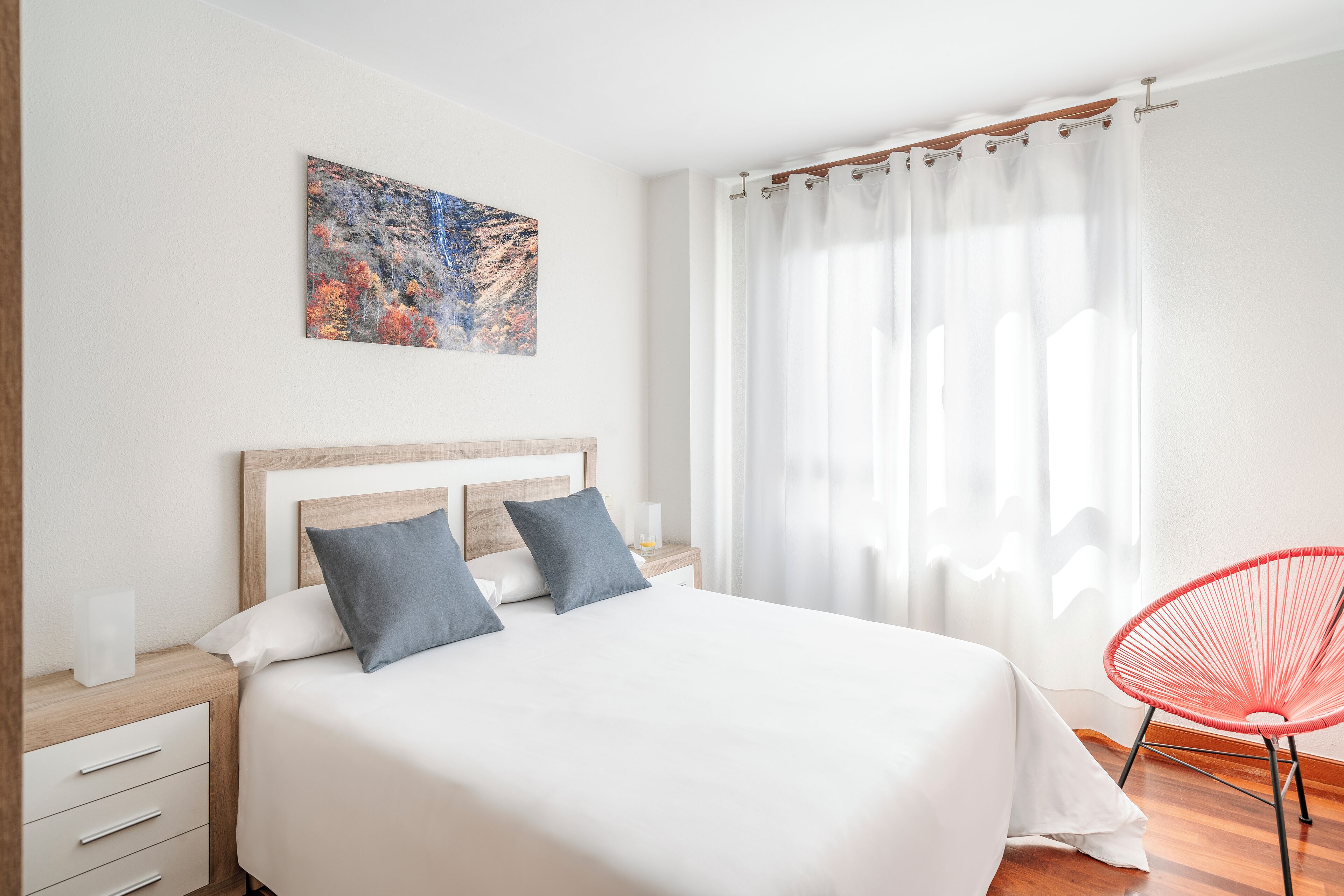 Une chambre à coucher bien rangée, avec un grand lit, une table de chevet, une chaise et un tableau accroché au mur.