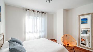 Habitació d'hotel amb un llit, una cadira, una finestra amb cortines i un mirall que reflecteix un llit.