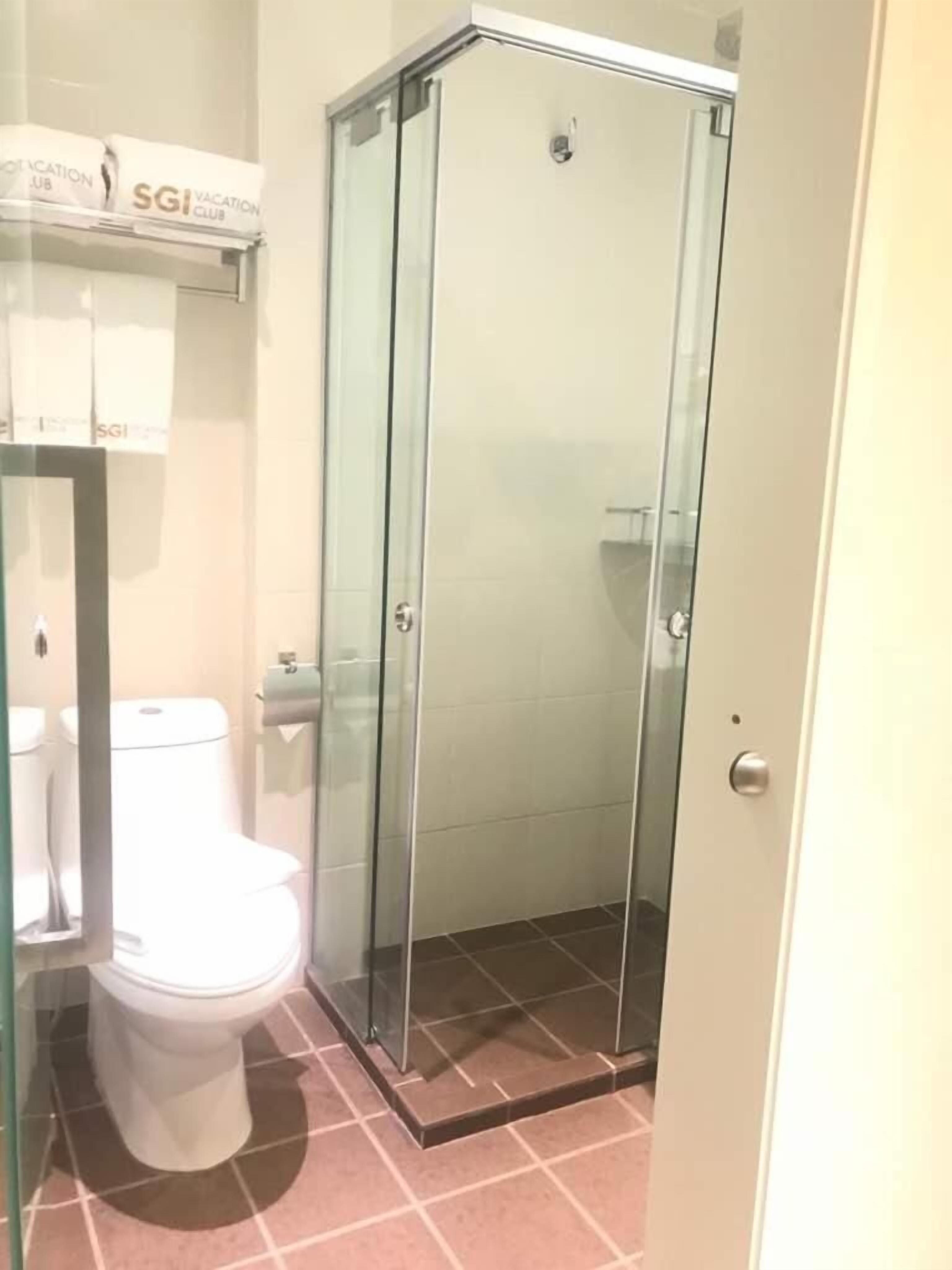 A bathroom with a glass-enclosed shower, a toilet, and a towel rack with a sign above it.