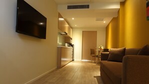 A modern living room with a flat-screen TV mounted on the wall, a brown sofa, and a dining area with a table and chairs.