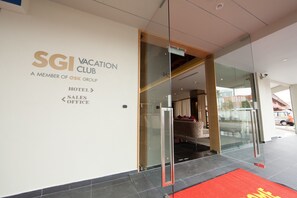 Entrada do hotel SGI Vacation Club, com porta de vidro, tapete vermelho e placa indicando as áreas de hotel, vendas e escritório.