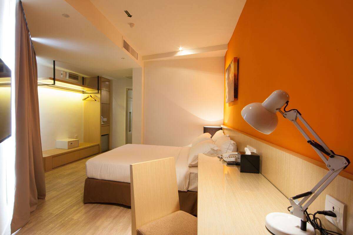 A hotel room with a bed, bedside table, lamp, and a mirror.