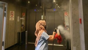A person using a steam cleaner in a hallway with glass doors and walls, and a no-smoking sign.