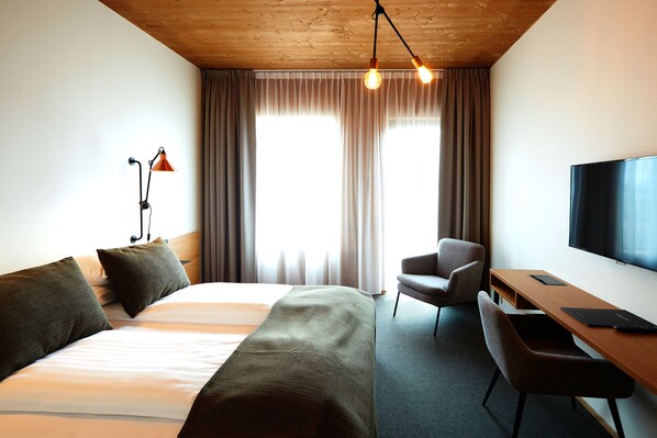 Una habitación de hotel con una cama grande, un escritorio con silla, televisión y una lámpara.
