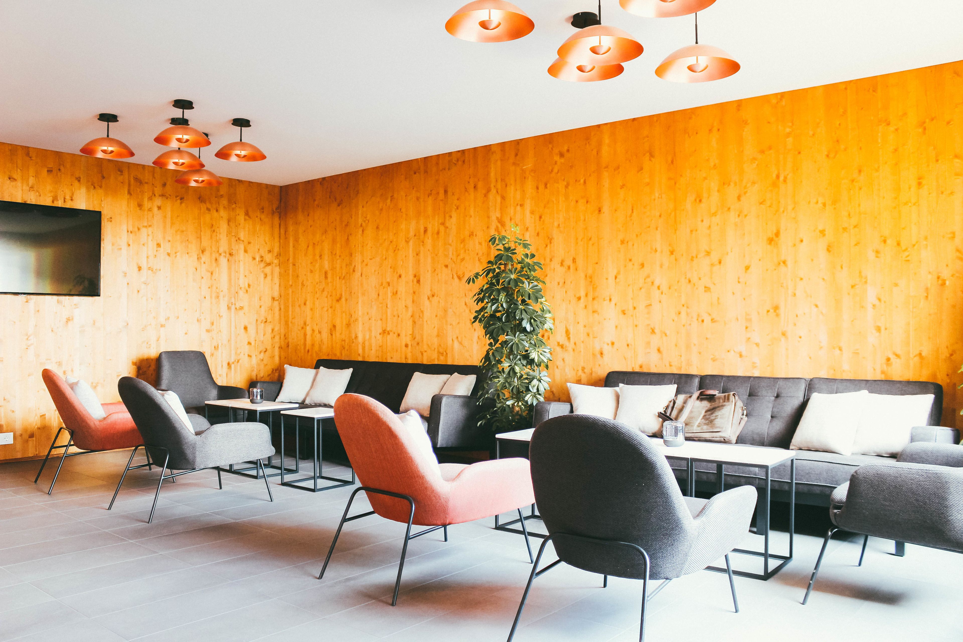 A modern interior with a wooden wall, a sofa, and multiple chairs arranged around a table.