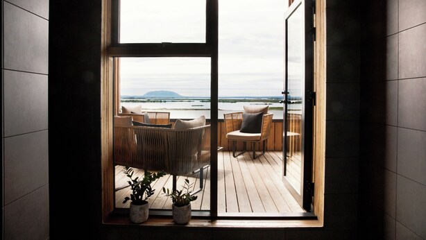 A room with a large sliding glass door leading to an outdoor deck with wicker furniture and potted plants. - Fosshotel Myvatn (Myvatn)