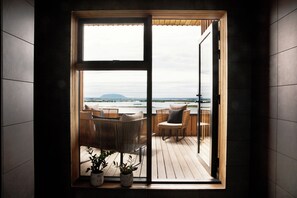 A room with a large sliding glass door leading to an outdoor deck with wicker furniture and potted plants. - Fosshotel Myvatn (Myvatn)