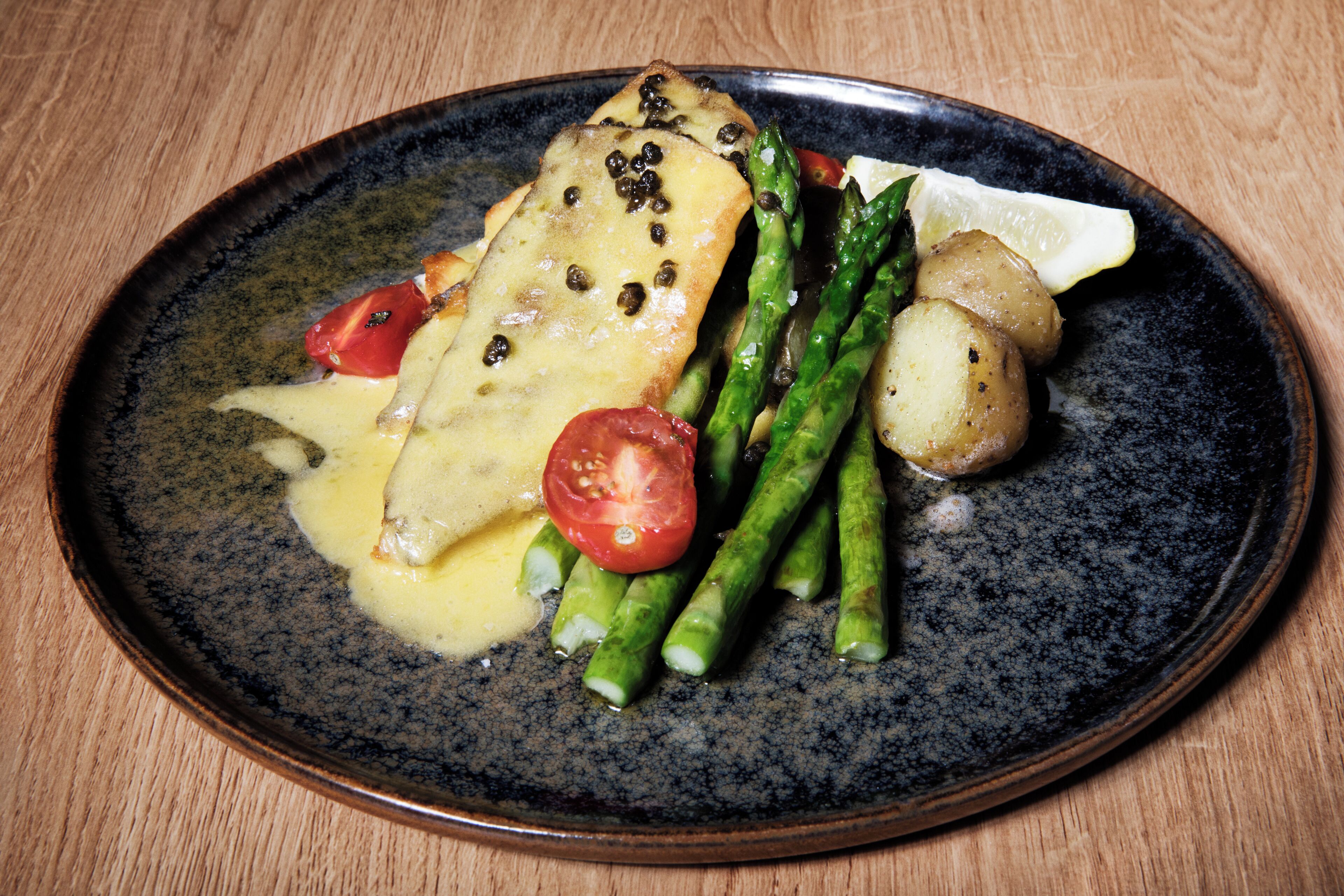 A plate with a fish fillet, asparagus, cherry tomatoes, and a lemon wedge.