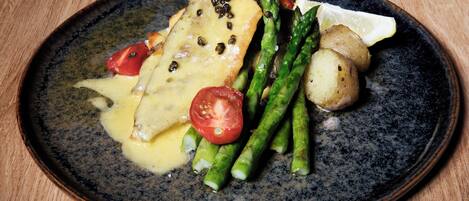 A plate with a fish fillet, asparagus, cherry tomatoes, and a lemon wedge.
