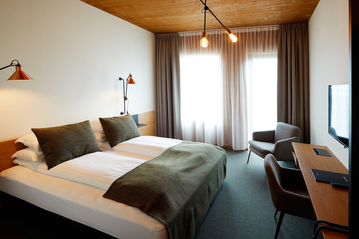 A hotel room with a bed, a desk, a chair, and a TV.