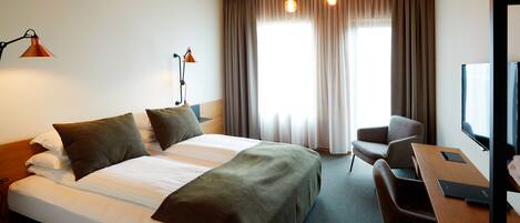 A hotel room with a bed, a desk, a chair, and a TV.