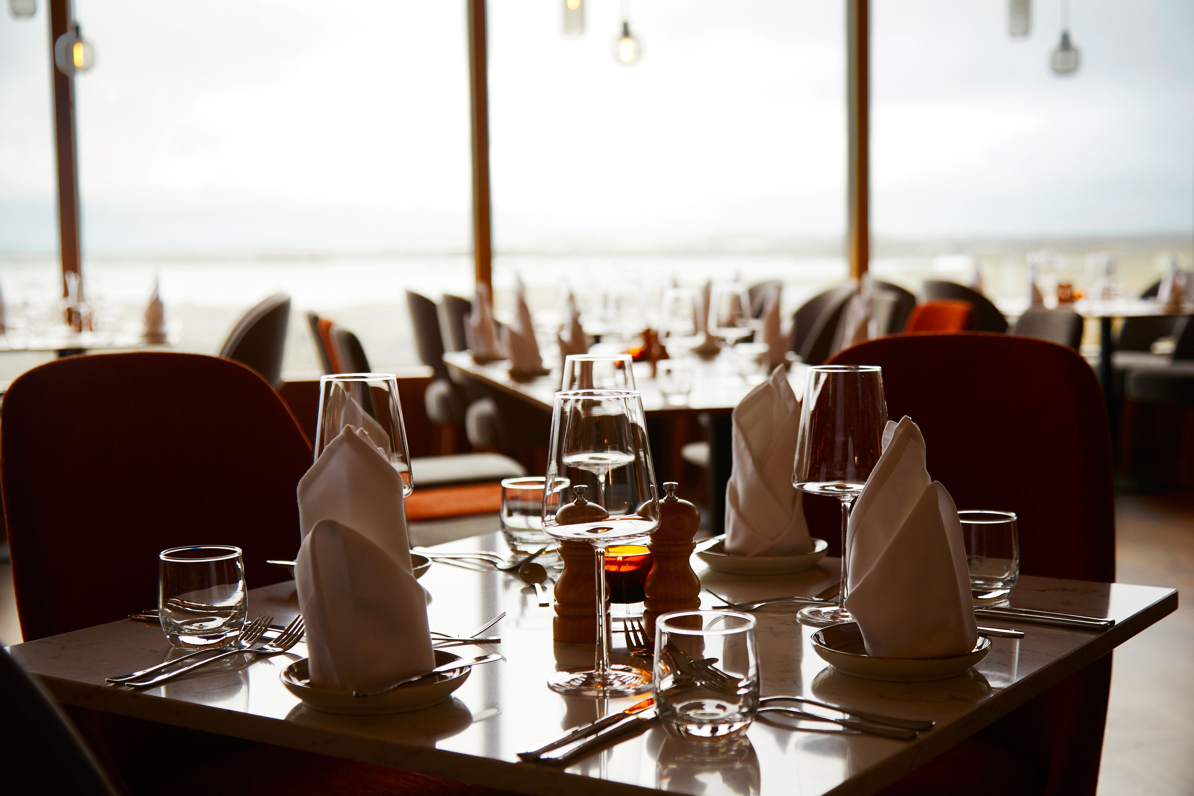 A dining table set with glasses, cutlery, and napkins, overlooking a body of water.