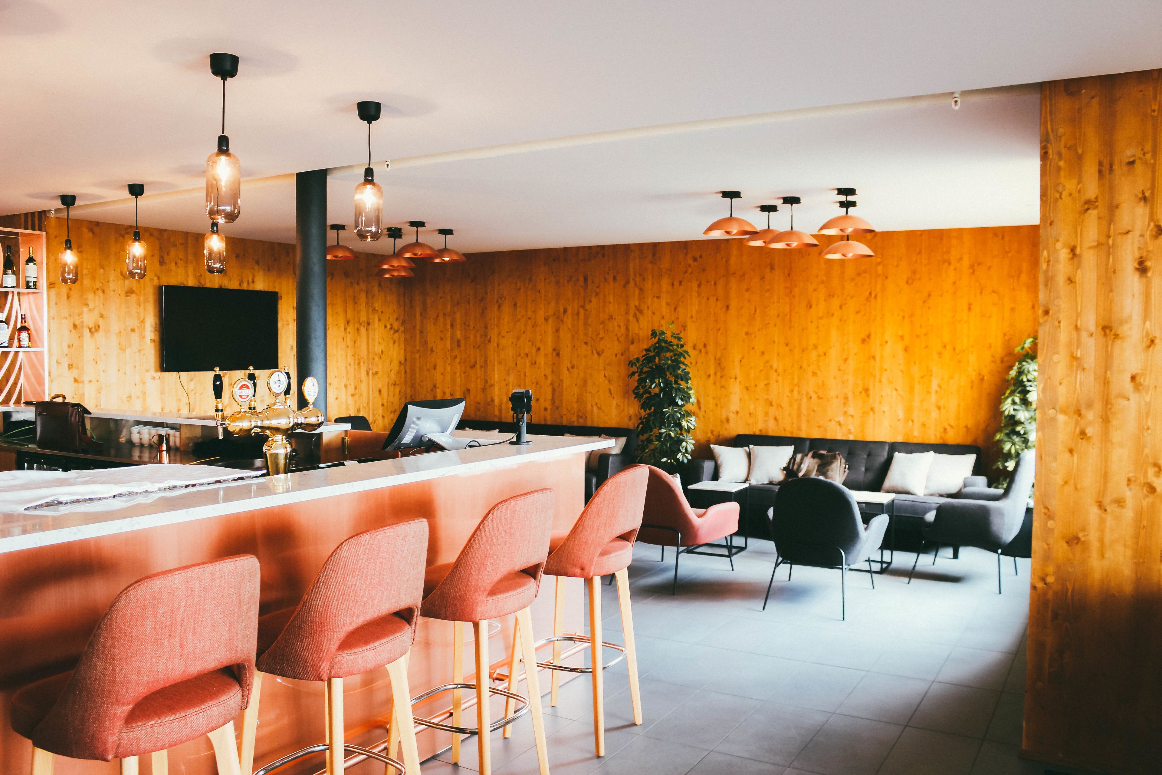 A modern bar area with a wooden accent wall, bar stools, and pendant lighting.