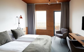 A modern hotel room with a large bed, a desk, and a chair. There is a window with curtains, a lamp, and a view of the outdoors.