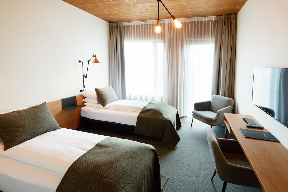 A hotel room with two beds, a desk, a chair, a TV, and a window with curtains.