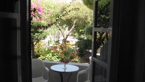 An open doorway leading to a small patio with a round table and two chairs, surrounded by lush greenery and flowering plants. - Eden Ios Rooms (Ios)