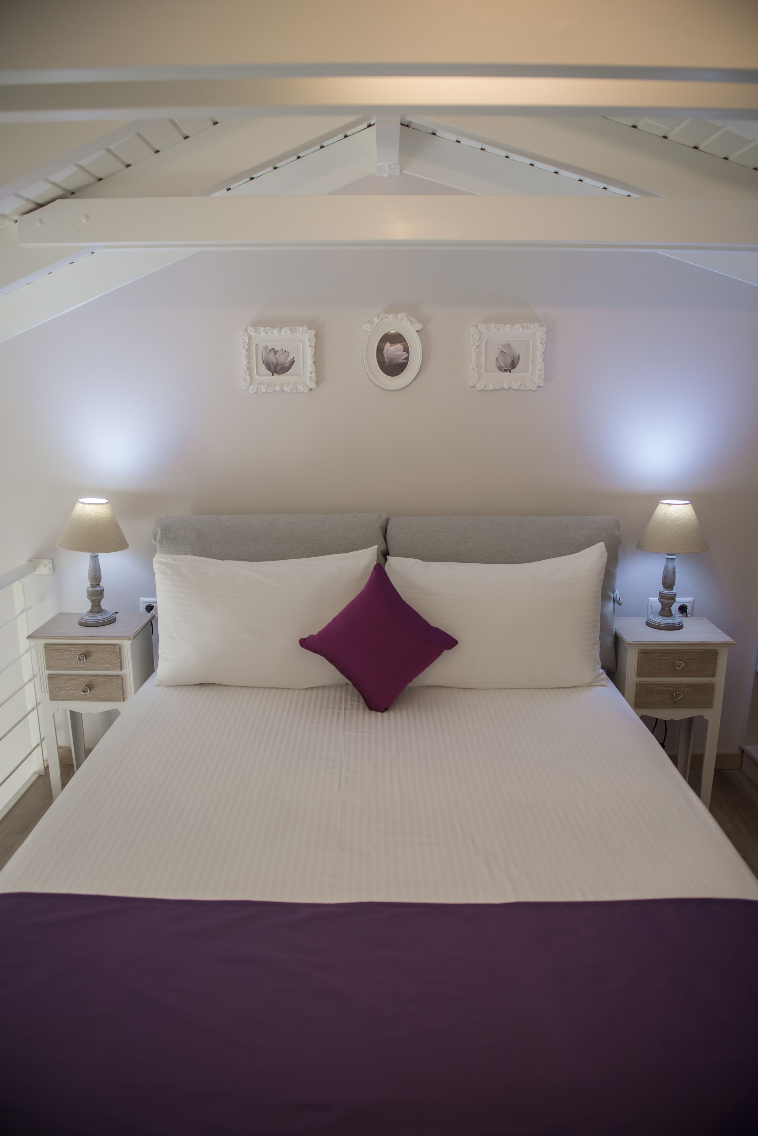 Une chambre à coucher avec un lit, deux tables de chevet et un plafond avec des poutres apparentes.