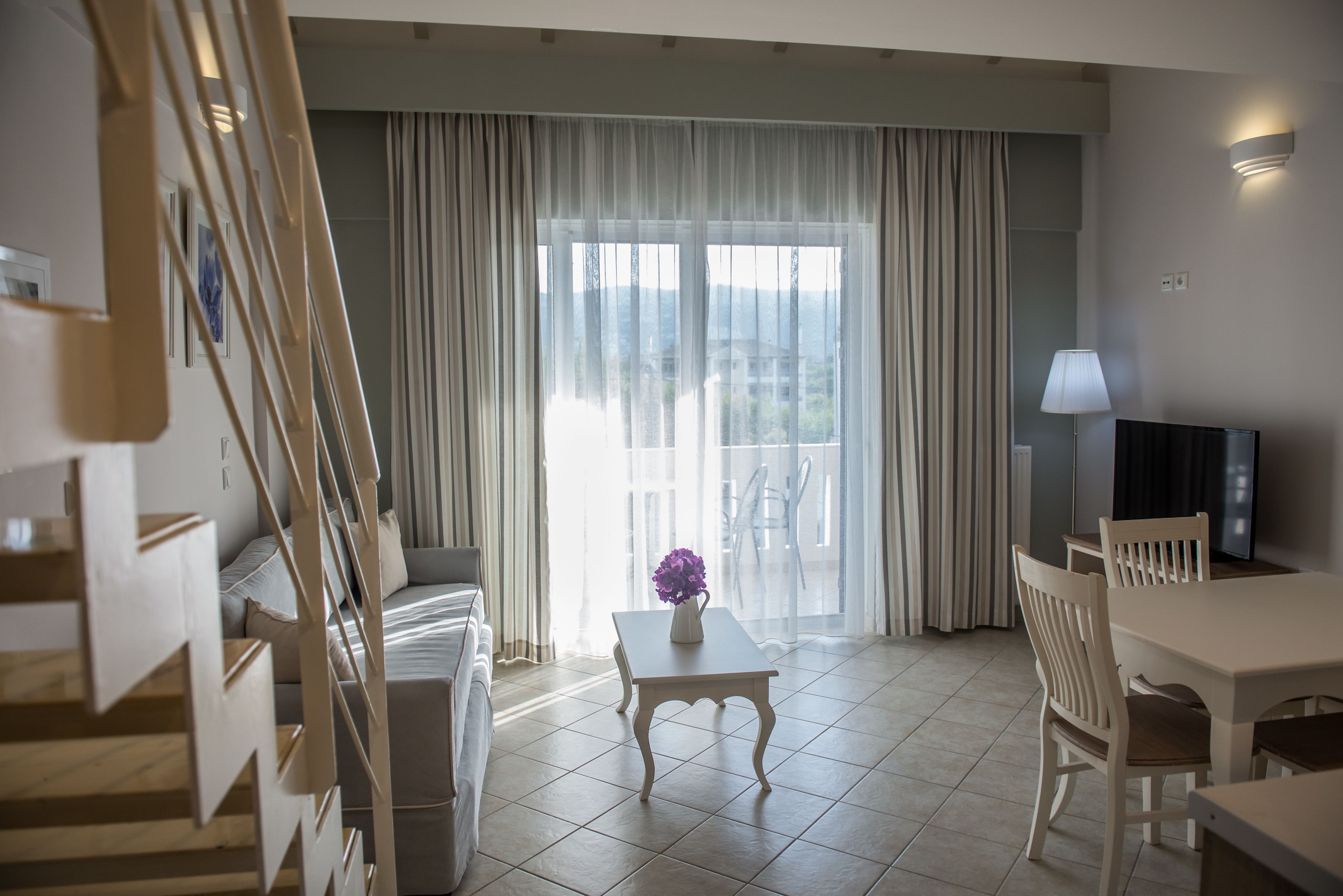Una sala de estar moderna con un sofá, una mesa con un jarrón, un televisor y una escalera.