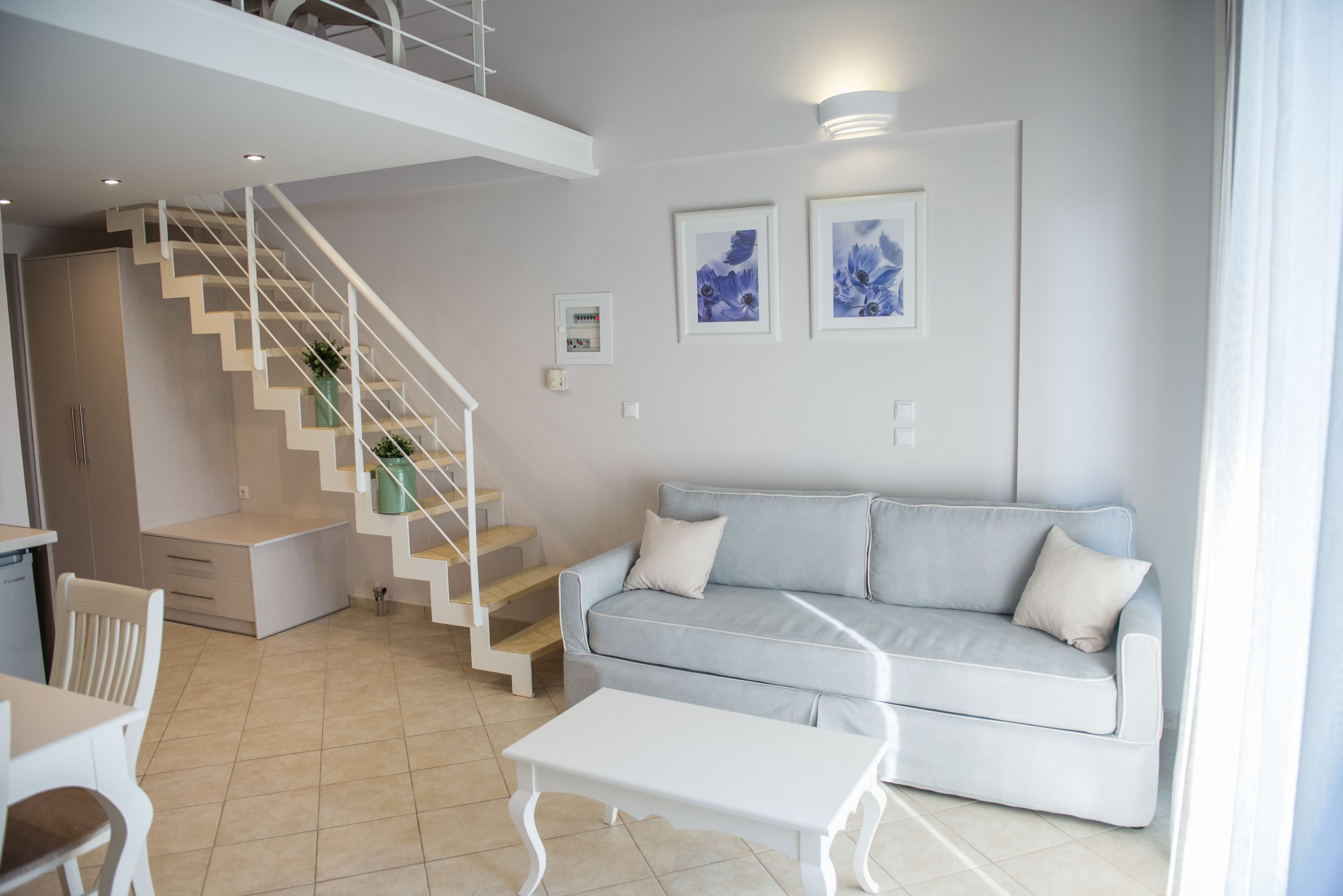 A modern living room with a staircase, a light grey sofa, and a white coffee table.
