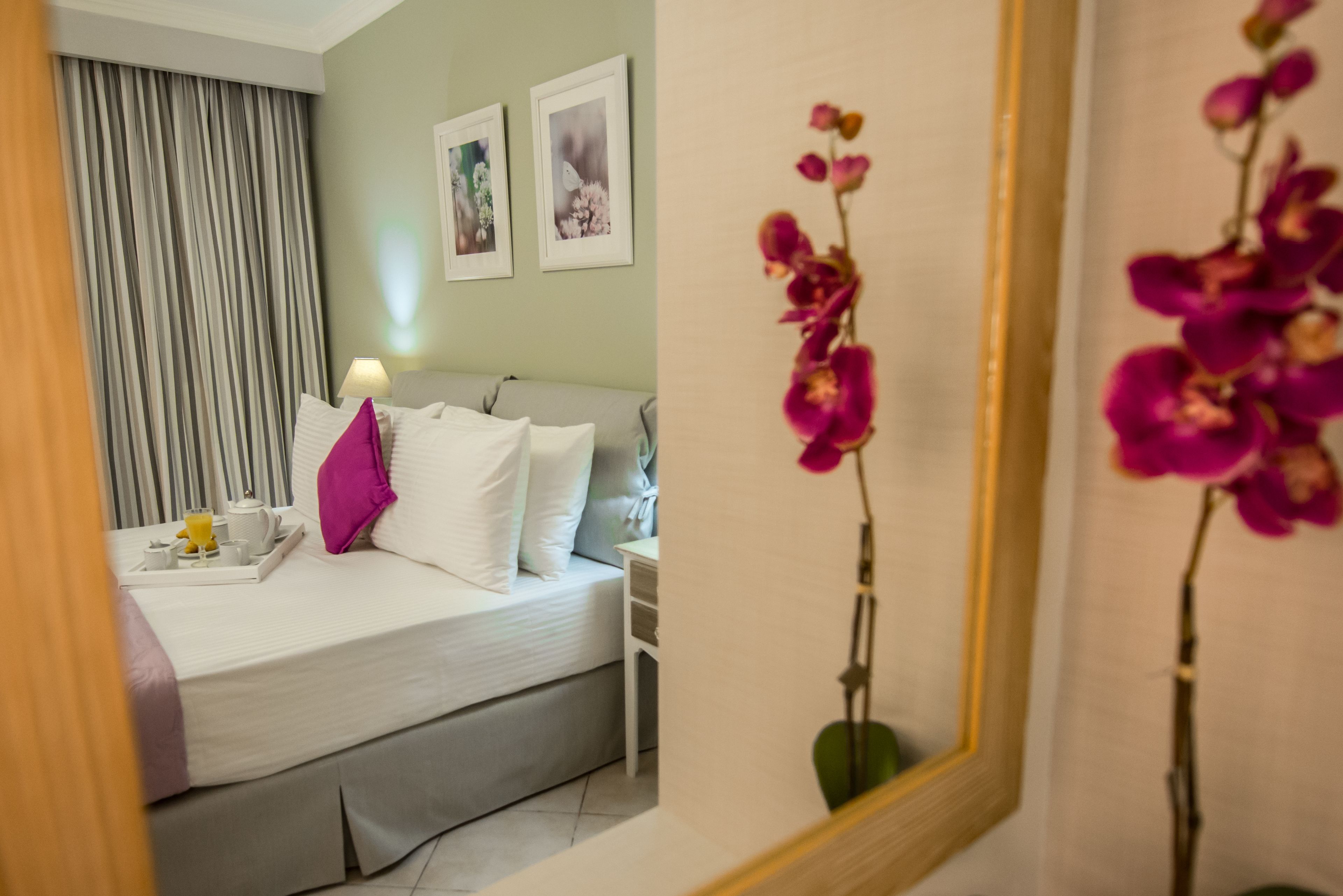 Quarto de hotel com cama, mesa de cabeceira, abajur e bandeja com uma xícara e um copo.