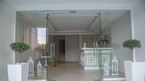 A modern hotel lobby with a glass entrance, white decor, and a staircase leading to the upper floors. - Lefkadio (Lefkada)