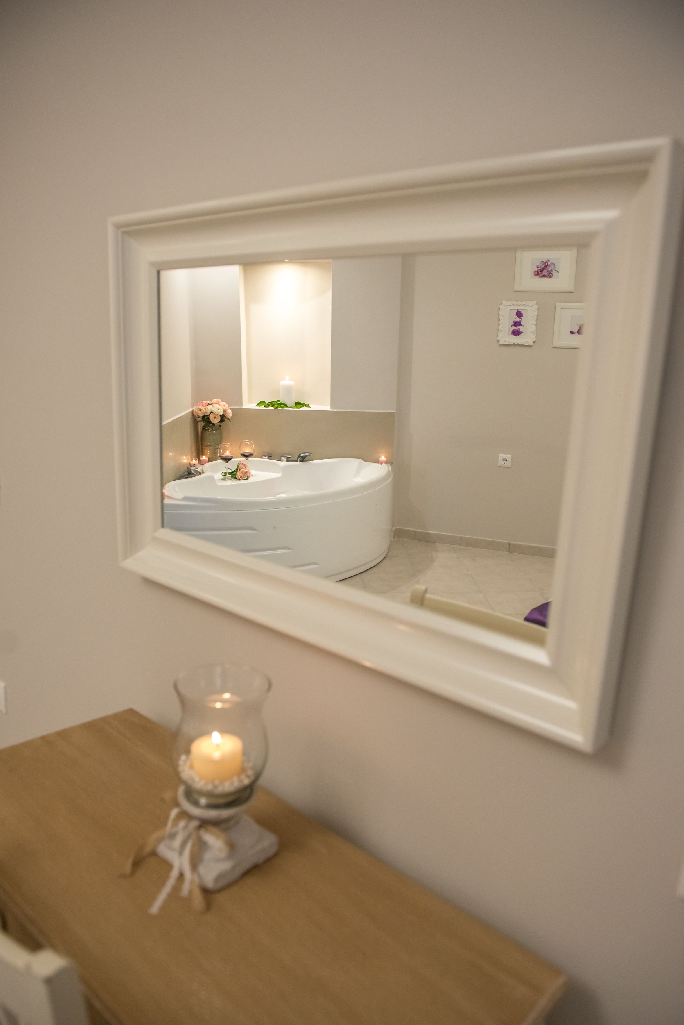 A bathroom with a white bathtub, a mirror, and a candle on a wooden table.