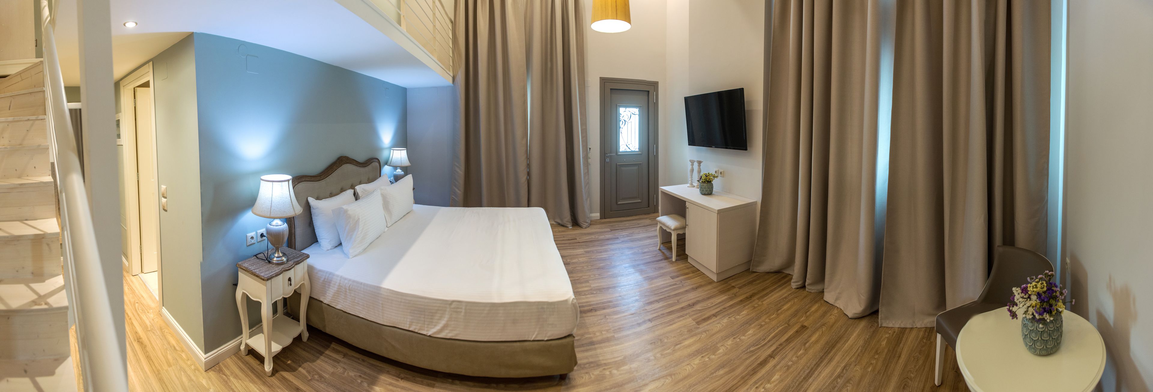 Een hotelkamer met een bed, nachtkastje met lamp, bureau met stoel, televisie en gordijnen.