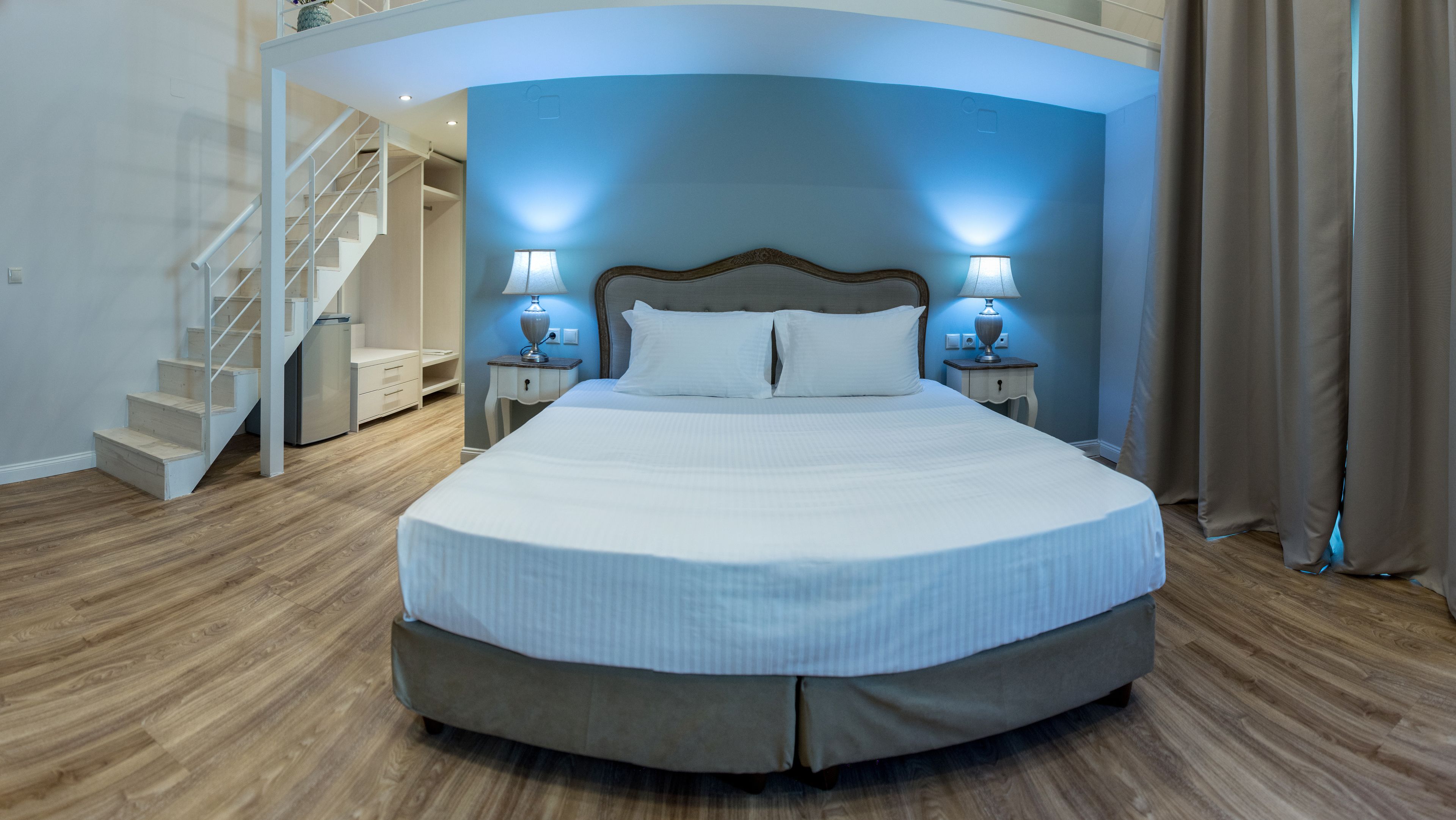A large bed with a headboard, two bedside tables with lamps, a wooden staircase, and a built-in closet.
