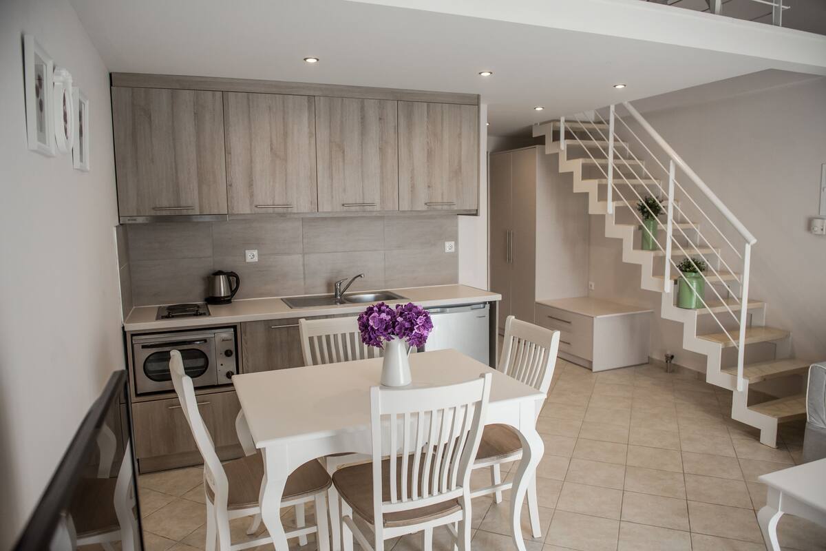 Una cocina moderna con armarios de madera, una mesa de comedor con sillas y una escalera.