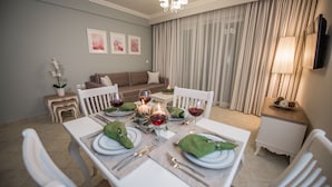 A dining area with a table set for four, including wine glasses, plates, and cutlery. There is a sofa in the background and a lamp on a side table. - Lefkadio (Lefkada)