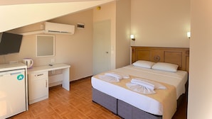 Quarto de hotel com uma cama, uma escrivaninha, uma televisão e um guarda-roupa.