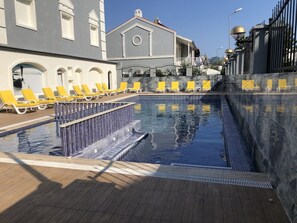 Una piscina al aire libre, sombrillas, sillones reclinables de piscina