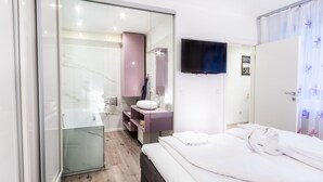Quarto moderno com cama, penteadeira com espelho e televisão na parede.