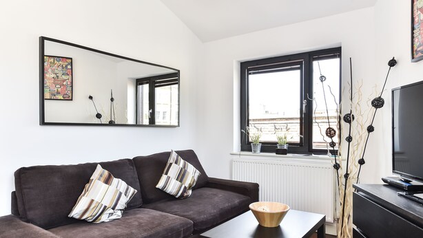 Ett modernt vardagsrum med en mörkbrun soffa, ett litet bord, en tv och ett fönster med utsikt över staden.