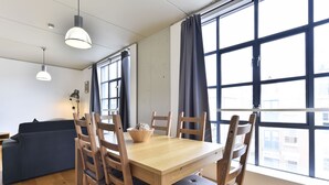 En matplats med ett träbord, sex stolar och en skål på bordet. I bakgrunden finns en mörk soffa och en golvlampa.