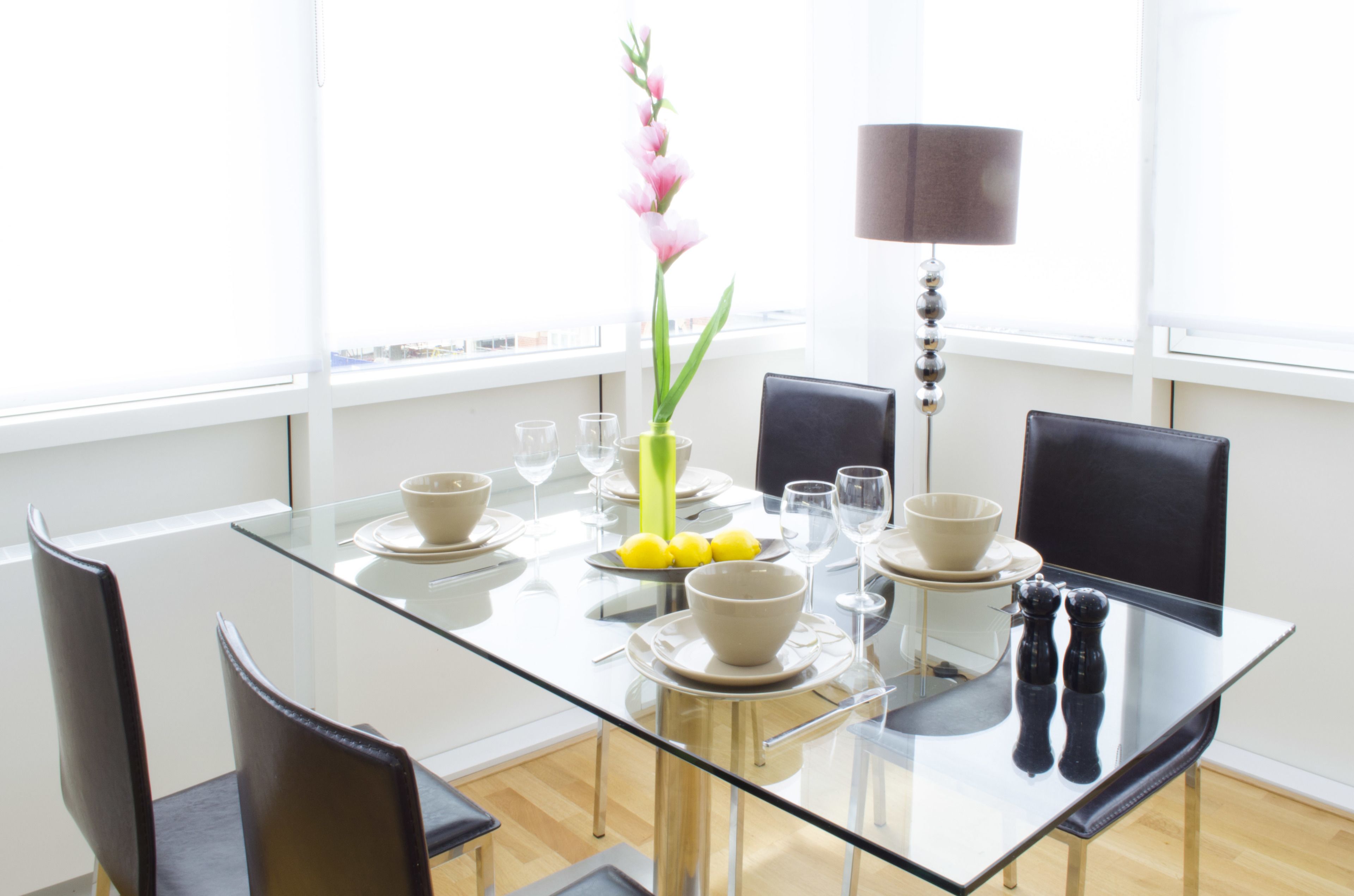 Un comedor moderno con una mesa de vidrio, sillas negras y un florero con flores.