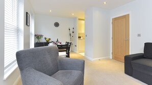 A living room with a grey sofa, a dining area with a table and chairs, and a wooden door. - Tower Bridge City Apartments (London)