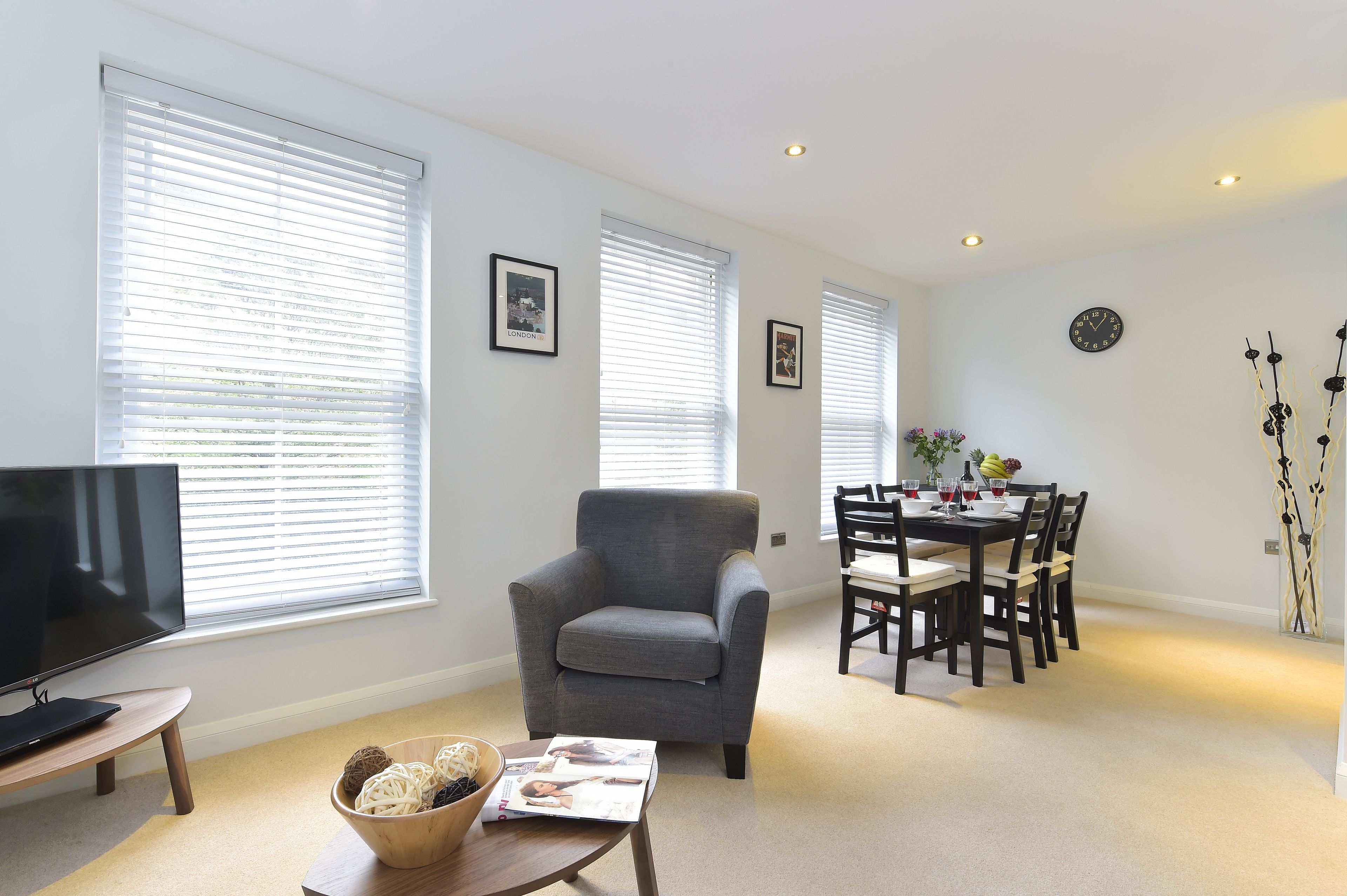 Una sala de estar con un sillón gris, un televisor y una zona de comedor con una mesa preparada para cuatro personas.