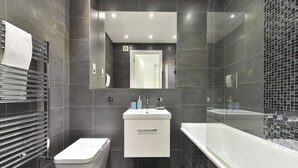 A modern bathroom with a toilet, sink, and bathtub. - Tower Bridge City Apartments (London)