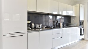 A modern kitchen with white cabinets, stainless steel appliances, and a black backsplash. - Tower Bridge City Apartments (London)