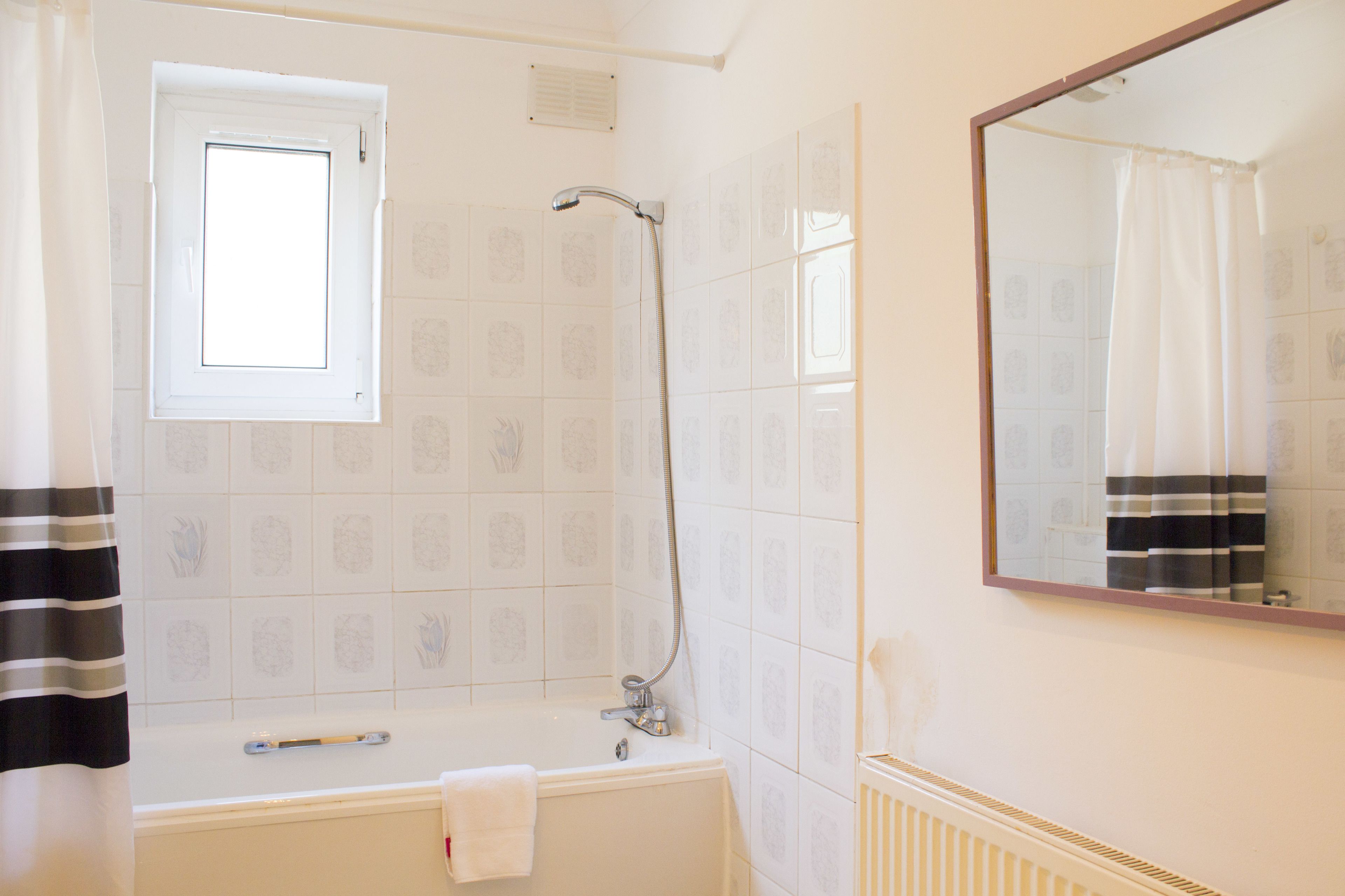 A bathroom with a bathtub, a shower, a window, and a mirror.