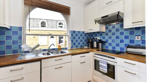 Eine moderne Küche mit weißen Schränken, einer Holz Arbeitsplatte, einer Edelstahl-Spüle und Blick auf ein Gebäude durch ein Fenster.