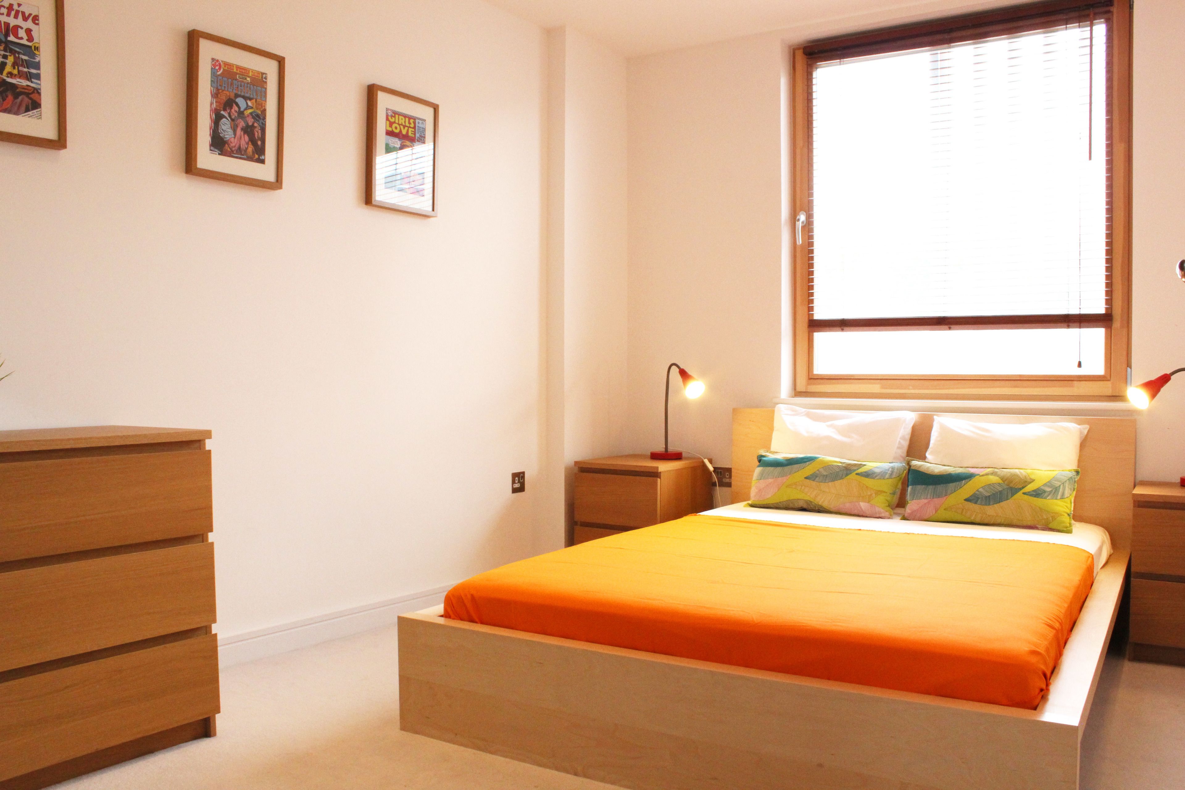 A bedroom with a bed, wooden dresser, nightstands, and framed pictures on the wall.