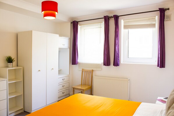 A bedroom with a bed, a wardrobe, a chair, and a window with curtains.