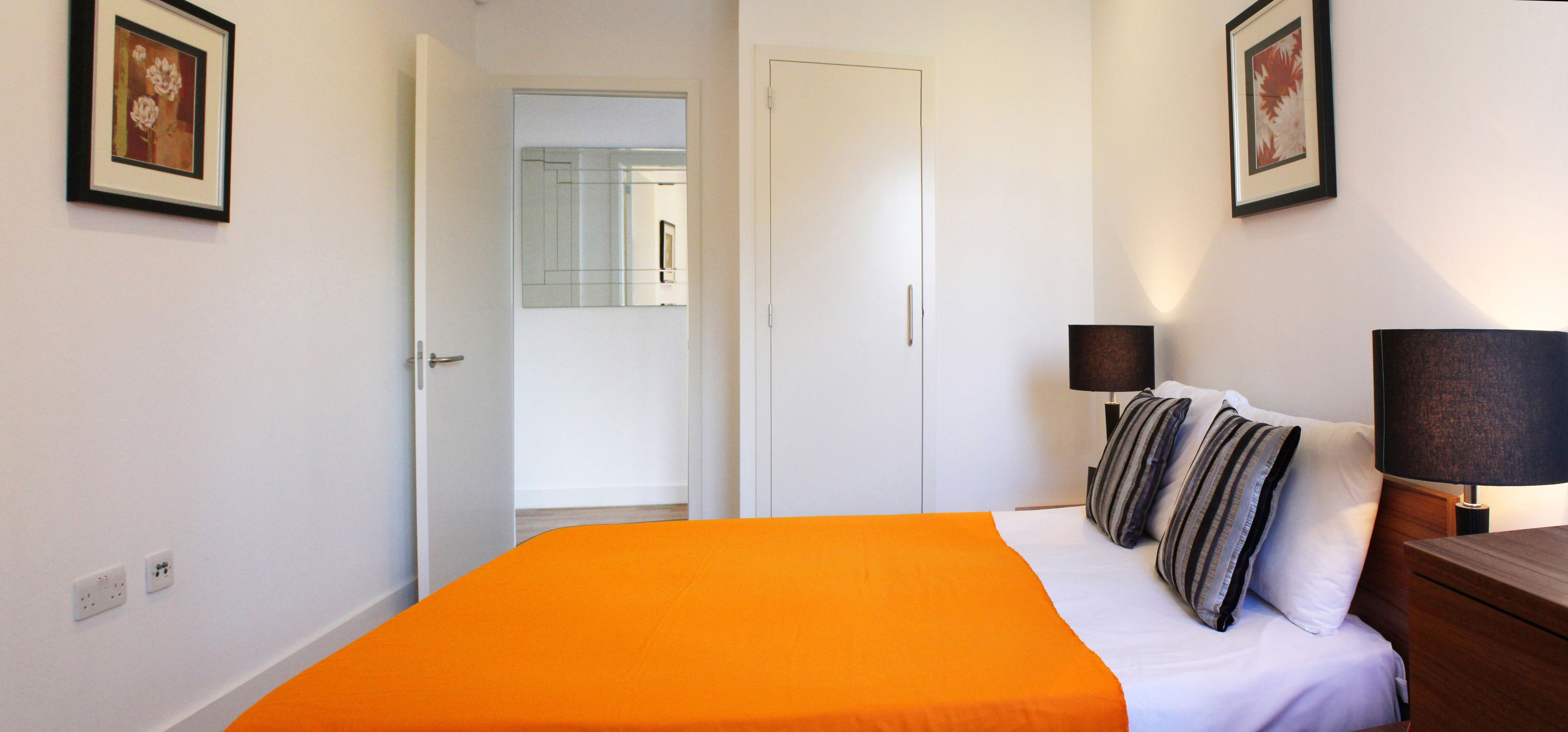A hotel room with a bed, a nightstand, a lamp, and a door leading to another room.