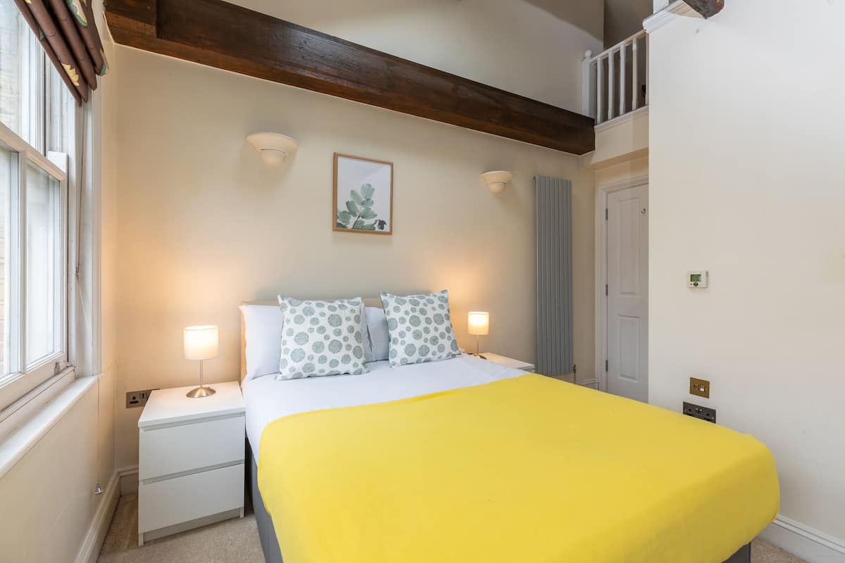 A hotel room with a bed, bedside lamps, a framed picture on the wall, and a window with curtains.